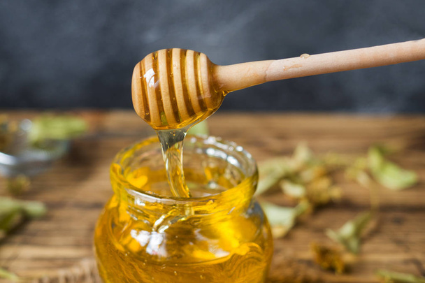 A jar of liquid honey from Linden flowers and a stick with honey on a dark background. - Foto, Imagem