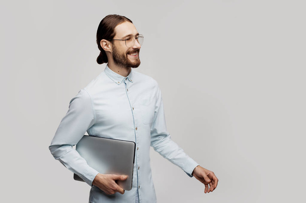 Genç gülümseyen iş adamı ayakta ve dizüstü bilgisayar kullanarak gri arka plan üzerinde izole. İyi ve mutlu görünüyor. Programlama projeleri için çok yeni fikirlerolması - Fotoğraf, Görsel