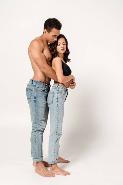 handsome mixed race man hugging attractive girl in lace bra and jeans on white  - Photo, image