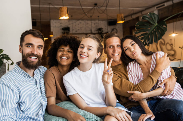 Happy multi ethnic young people looking at camera, smiling diverse friends or students showing peace sign, multicultural millennials posing together at meeting, tolerance and racial equality concept  - Photo, Image