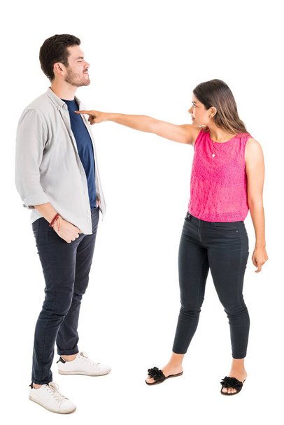 Volledige lengte van Hispanic geërgerd vrouw wijzend op vriendje terwijl vechten tegen witte achtergrond - Foto, afbeelding