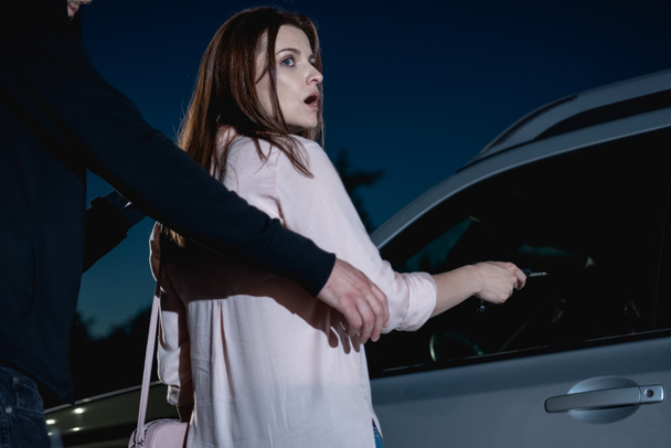 thief attacking frightened woman from behind near car - Zdjęcie, obraz