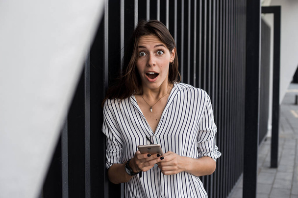 Χαρούμενη νεαρή γυναίκα διαβάζοντας το μήνυμα από το φίλο στο κινητό εκφράζοντας την ευτυχία για τα καλά νέα, συναισθηματική γυναίκα ενθουσιασμένος με τη νίκη έκπτωση για τα ψώνια, ενώ το περπάτημα στο κέντρο της πόλης - Φωτογραφία, εικόνα