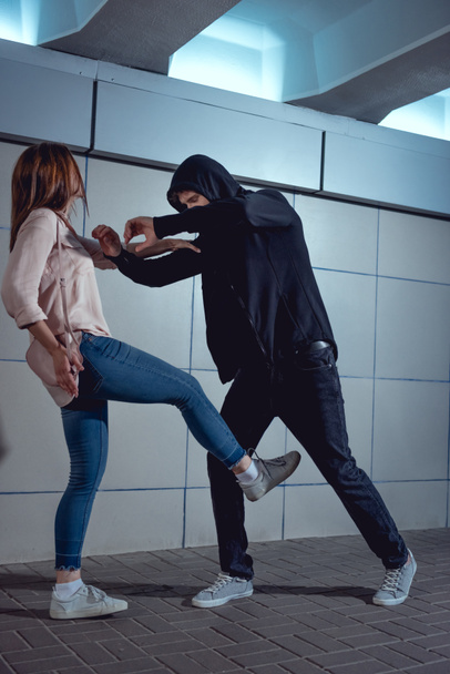 woman defending herself from attacking thief in black hoodie in underpass - Foto, immagini