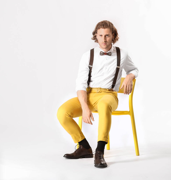 Stylish young man sitting on chair against white background - Foto, afbeelding