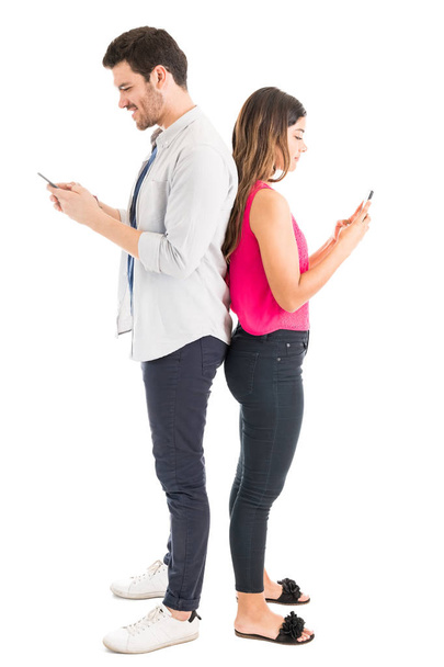 Atractivas parejas hispanas enviando mensajes de texto en sus teléfonos inteligentes mientras están de espaldas en el estudio
 - Foto, Imagen