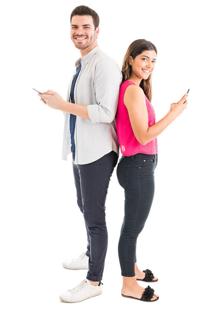 Longitud completa del hombre y la mujer sonrientes utilizando teléfonos móviles sobre fondo llano
 - Foto, Imagen