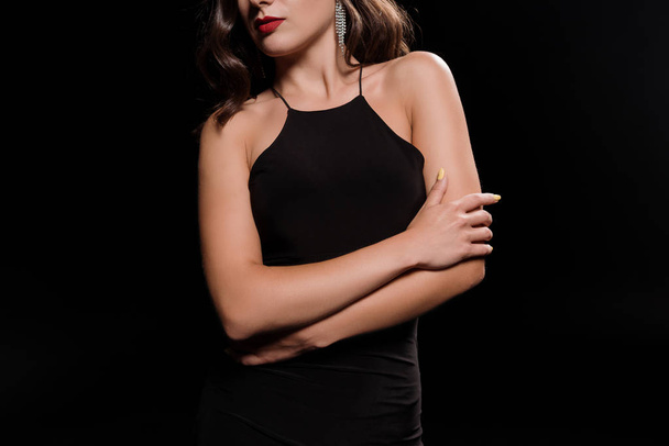 cropped view of young woman in dress standing with crossed arms isolated on black  - Foto, Imagen