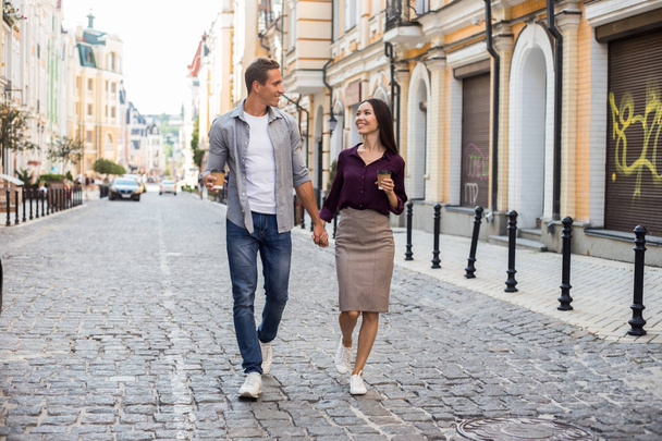 Positive multiracial couple walking together, stroll during weekends, drink takeaway coffee, stand near fence, have pleasant talk with each other, Valentine's Day. People and lifestyle concept - Valokuva, kuva