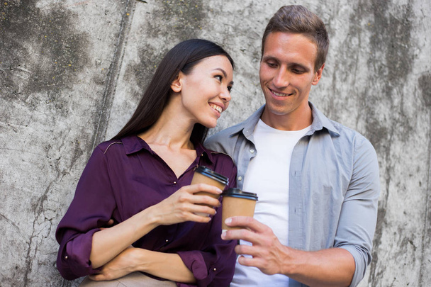 Hurry for meeting. Two young business people walking outside on the city street drinking hot coffee talking smiling joyful close-up. Romantic relationship, love affair at work - 写真・画像