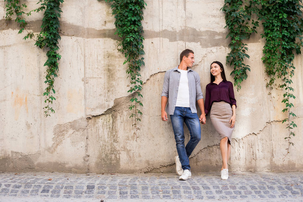 Young attractive romantic tourist couple, adult European handsome man and asian woman standing together at double tandem on grey street wall background. Copyspace for advertising, logo, text or copy  - Zdjęcie, obraz