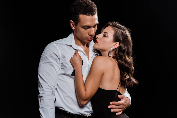 beautiful woman embracing handsome mixed race man isolated on black  - Fotó, kép