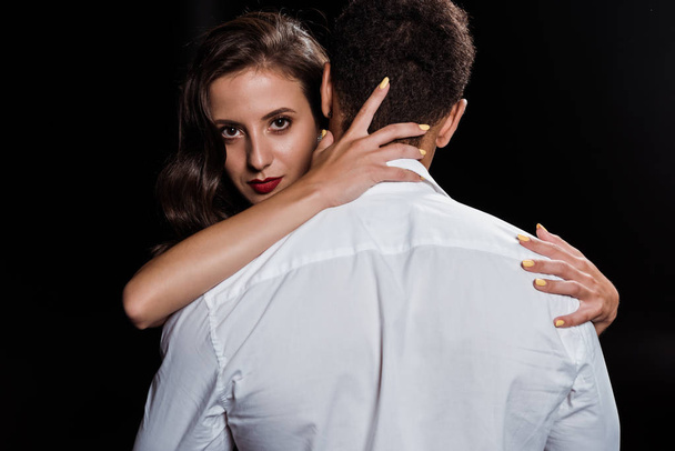 woman hugging man and looking at camera isolated on black  - Photo, Image
