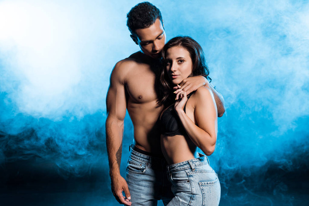 handsome mixed race man holding hands with sexy girl on blue with smoke  - Foto, Bild