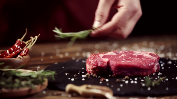 Viljelty näkymä mies hankaa raakaa lihaa pihvi rosmariini lähellä ainesosia pöydällä
 - Materiaali, video