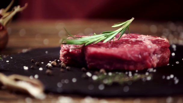 vallende rozemarijn op rauwe vlees steak op tafel met ingrediënten - Video
