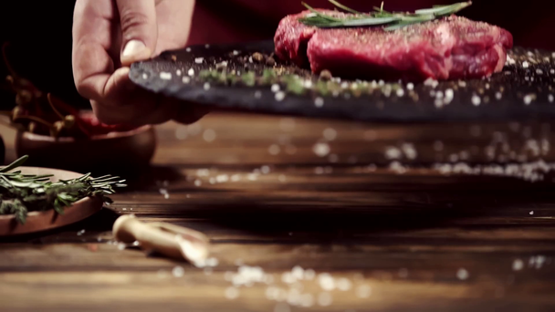 Bijgesneden beeld van de mens nemen plaat met rauwe vlees steak versierd met specerijen en rozemarijn geïsoleerd op zwart - Video