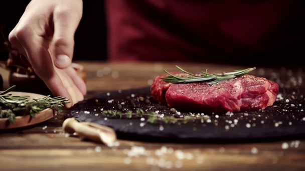 Viljelty näkymä mies laittaa pöydälle lautaselle raakaa lihaa pihvi koristeltu mausteet ja rosmariini eristetty musta
 - Materiaali, video