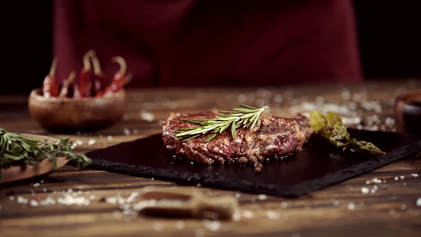 falling rosemary on delicious meat steak on table with ingredients - Footage, Video