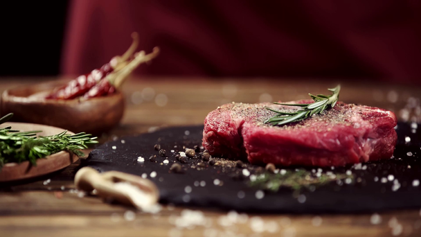 vallende specerijen op rauwe vlees steak op tafel met ingrediënten - Video
