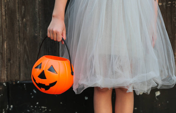 Smiling blond girl holding Halloween pumpkin jack o'lantern with sweet candy in hands on wooden background. Halloween celebration concept. - Fotoğraf, Görsel