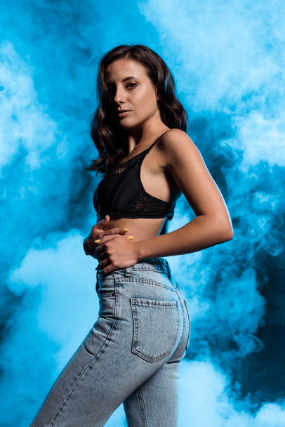 junge Frau in Spitzen-BH und Jeans auf blau mit Rauch  - Foto, Bild