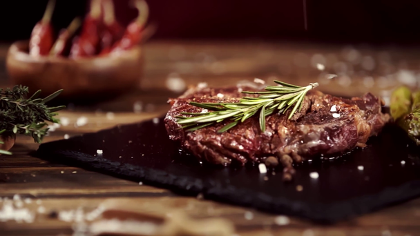 падіння солі на смачний стейк м'яса на столі з інгредієнтами - Кадри, відео