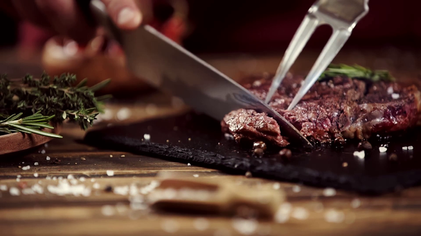 Przycięte widok człowieka cięcia stek z mięsa ze sztućcami na stole - Materiał filmowy, wideo
