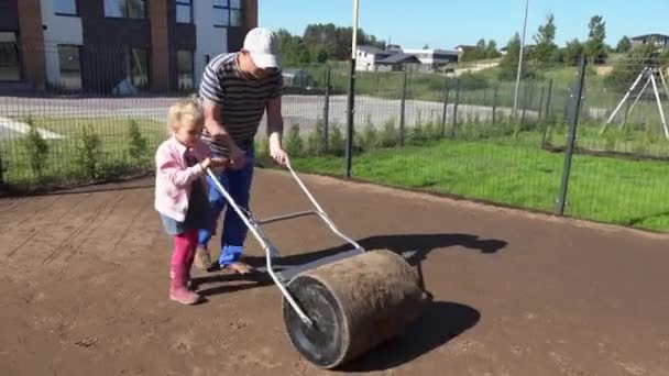Father and helper girl level ground with roller in townhouse yard. lawn seeding. - Footage, Video