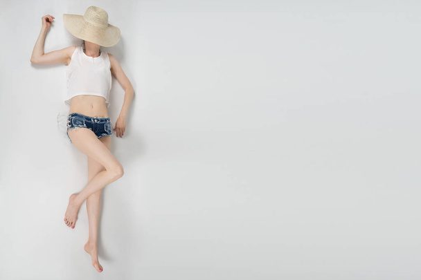 the girl in shorts and hat covering her face lying on white background isolated - Foto, Imagen