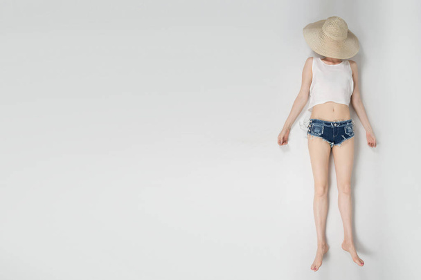 the girl in shorts and hat covering her face lying on white background isolated - Valokuva, kuva