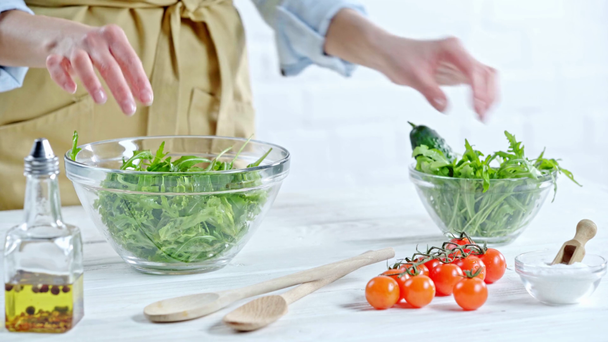 テーブルの上の食材の近くに野菜サラダにルッコラを入れる女性のトリミングビュー - 映像、動画