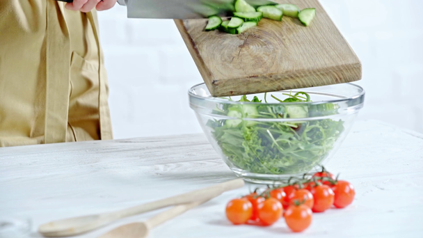 Vista cortada de mulher que põe pepinos na salada vegetal perto de ingredientes na mesa
 - Filmagem, Vídeo