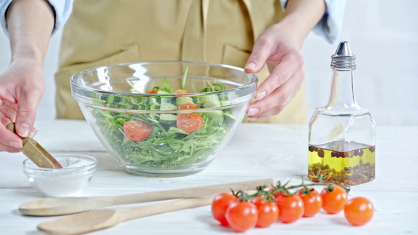 Обрезанный вид женщины, приправляющей овощной салат солью рядом с ингредиентами на столе
 - Кадры, видео