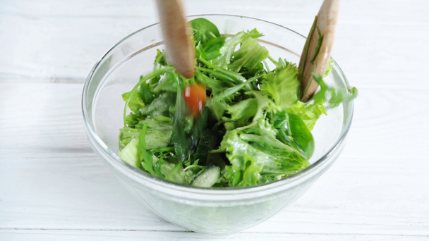 Oříznutý pohled na ženu míchání zeleninového salátu v nádobě s dřevěnými špachty  - Záběry, video