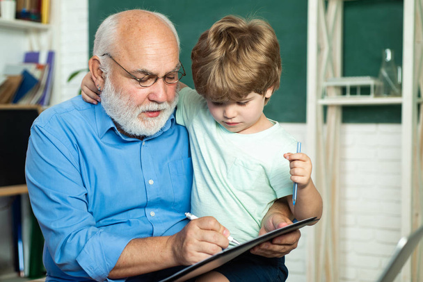 Cute little preschool kid boy with Grandfather in a classroom. Boy from elementary school at the school yard. A grandfather and a toddler are learning in class. Little ready to study. - Φωτογραφία, εικόνα