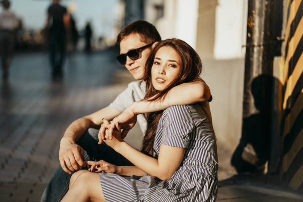 Happy young couple in love teenagers friends dressed in casual style sitting together on city street - Photo, Image