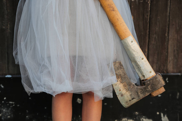 Sorrindo menina loira segurando um machado em mãos sobre fundo de madeira. Celebração de Halloween, conceito de horror
. - Foto, Imagem