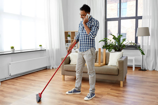 man with broom cleaning and calling on smartphone - Foto, afbeelding