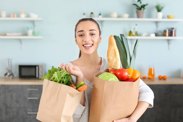 Beautiful woman with shopping bags full of fresh products in kitchen at home - Photo, Image