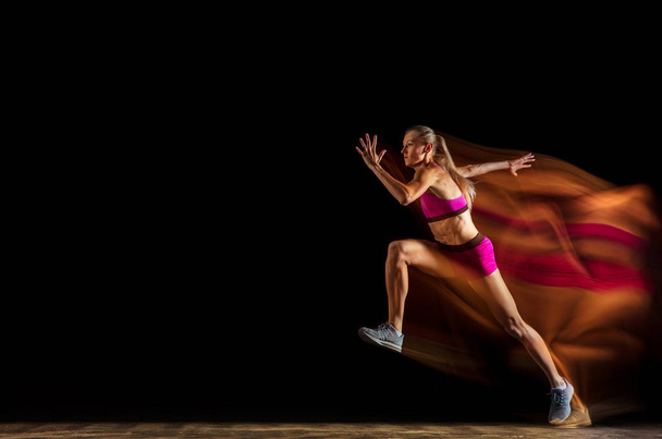 Professionele vrouwelijke estafette racer training op zwarte studio achtergrond in gemengd licht - Foto, afbeelding