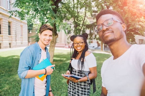 Oktatás, életmód, szabadidő és technológiai koncepció. Soknemzetiségű diákok sugárzó mosoly is pózol a selfie shot kültéri egyetemi campus Park. V. tükrözte hatás. - Fotó, kép