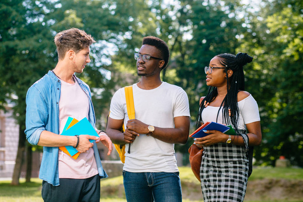 Egy fekete nő a szemüveg és két diák többnemzetiségű férfi beszél kültéri egyetemi campus. Barátság koncepció. - Fotó, kép