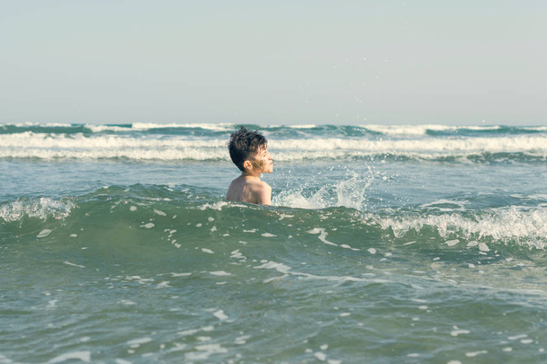 Boy on beach In Sea Waves with Water Splashes. Concept of summer vacation - Фото, зображення
