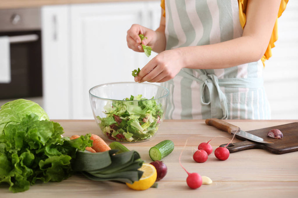 Beautiful woman preparing tasty vegetable salad in kitchen at home - Foto, Imagem