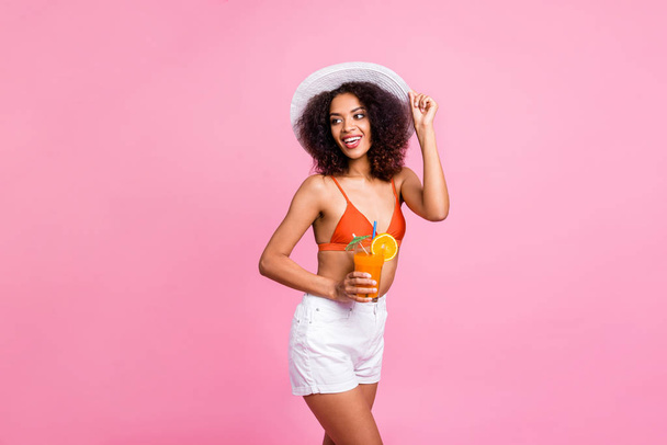 Close up side profile photo bright beautiful she her dark bronze skin model lady hold hands arms fresh cold juice beverage walk seaside ocean wear sun hat swimming orange suit isolated pink background - Foto, immagini