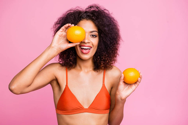Close up photo bright beautiful funny toothy she her dark bronze skin model lady hold hands arms hide eye fresh exotic fruit citrus food eat wear swimming orange suit isolated pink background - Valokuva, kuva