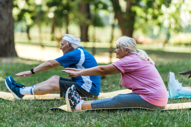 enfoque selectivo de la mujer mayor con el pelo gris y el hombre haciendo ejercicio en fintess esteras en la hierba
  - Foto, Imagen