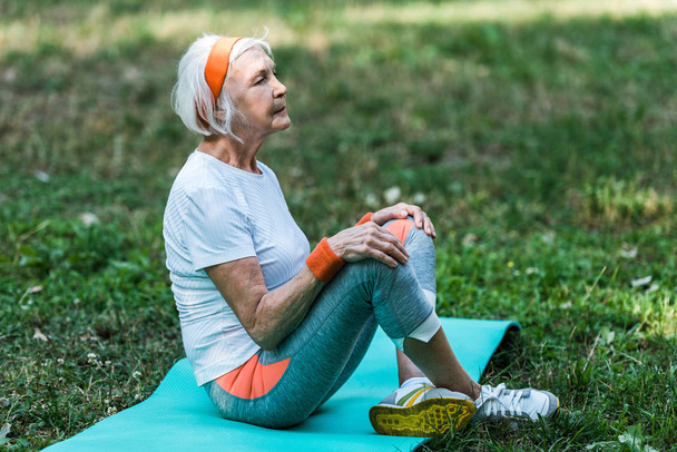 senior woman in sportswear sitting with crossed legs on fitness mat  - Photo, Image