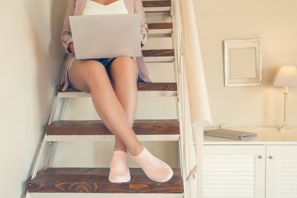 Girl student in shorts sits on the steps with a laptop in a cafe in the home style and pastel colors - Fotó, kép